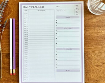 May include: A daily planner notepad with a lavender border and the words "DAILY PLANNER" at the top. The notepad has sections for time, schedule, date, goals, to-do list, and notes. Two purple pencils and a sprig of lavender are next to the notepad.