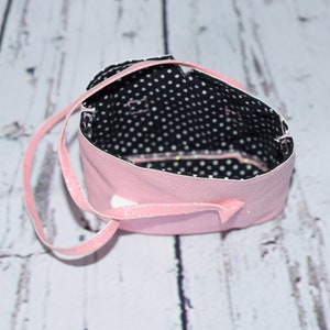 May include: A pink fabric bag with a black and white polka dot lining. The bag has a single strap and is made of a soft, sparkly fabric.