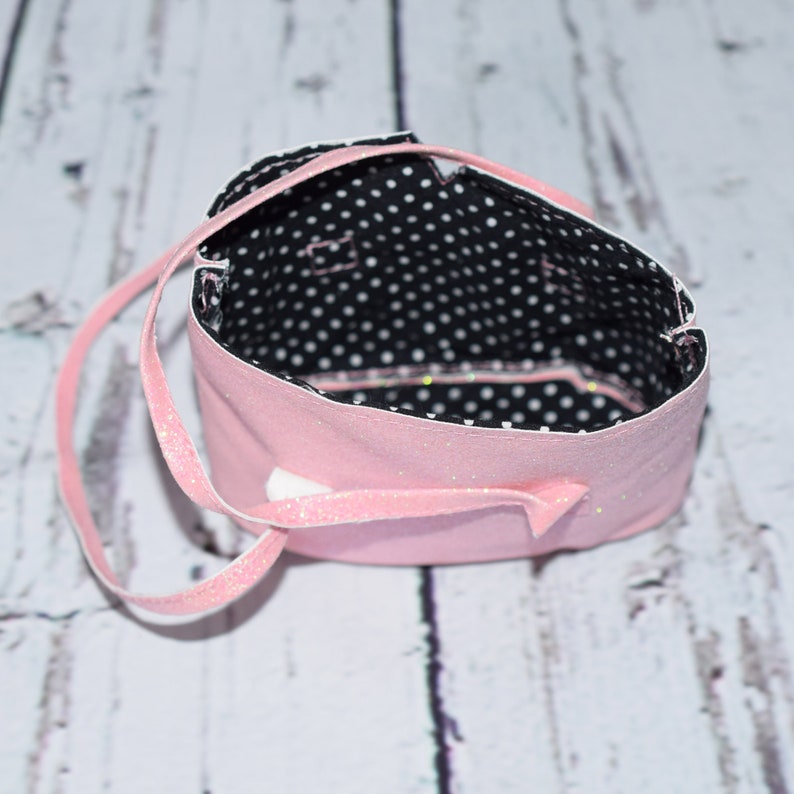 May include: A pink fabric bag with a black and white polka dot lining. The bag has a single strap and is made of a soft, sparkly fabric.