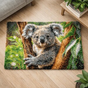Könnte beinhalten: Ein rechteckiger Teppich mit einem detaillierten Bild eines Koala-Bären, der sich an einem Baum festhält. Das Design des Teppichs enthält Grautöne, Braun und Grün, wodurch ein strukturierter, dreidimensionaler Effekt entsteht. Das Fell des Koalas und die Baumrinde sind detailliert dargestellt.