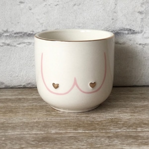 Könnte beinhalten: Weiße Keramiktasse mit einem rosa Umriss einer Büste und zwei goldenen Herzen.