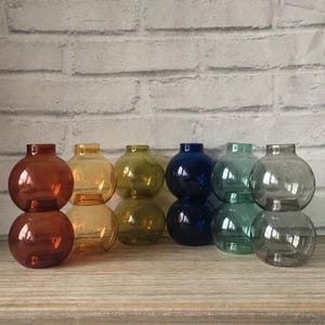 May include: Set of ten glass bud vases in various colours, including amber, green, blue, and grey. The vases are round and have a bulbous shape.