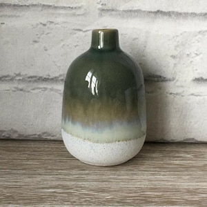 Könnte beinhalten: Eine Keramikvase mit rundem Körper und schmalem Hals. Die Vase hat eine Farbverlaufsoptik, die von einem dunklen Grün oben zu einem gesprenkelten Weiß am Boden übergeht. Die Vase ist etwa 18 cm hoch.