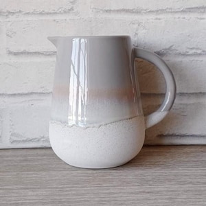 May include: A grey ceramic jug with a white glaze and a textured base. The jug has a wide mouth and a handle.