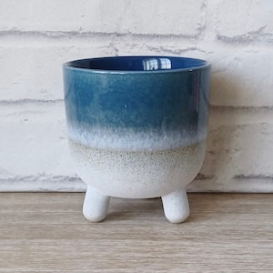 Könnte beinhalten: Ein blauer und weißer Keramiktopf mit drei Beinen. Der Topf hat ein Farbverlaufsdesign, das von einem dunklen Blau zu einem hellen Blau und dann zu einer weißen Basis übergeht.