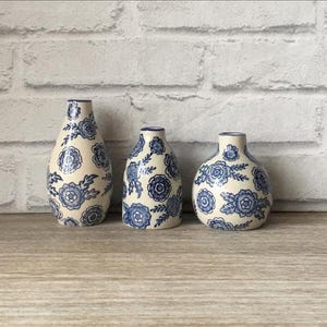 May include: Three ceramic vases with a cream base and blue floral patterns. The vases vary in size and shape, with a rounded, bulbous form. The blue floral design includes stylized flowers and leaves, creating a classic, decorative look.
