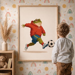 Peut inclure: Une impression d'art encadrée représentant une grenouille verte portant un sweat à capuche rouge et un short de sport bleu, frappant un ballon de football noir et blanc. La grenouille est représentée dans une pose dynamique sur fond clair.