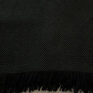 Puede incluir: Bufanda verde oscuro con un patr&oacute;n de espiga tejido y flecos en el borde inferior. La bufanda est&aacute; hecha de un material grueso y texturizado.