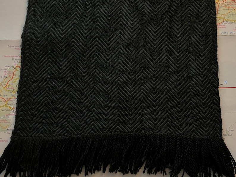 Puede incluir: Bufanda verde oscuro con un patr&oacute;n de espiga tejido y flecos en el borde inferior. La bufanda est&aacute; hecha de un material grueso y texturizado.