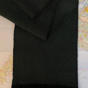 Puede incluir: Una bufanda verde oscuro con un dise&ntilde;o de espiga y un borde con flecos. La bufanda est&aacute; doblada, mostrando el tejido detallado. La bufanda est&aacute; hecha de un material suave y es adecuada para el clima fr&iacute;o.