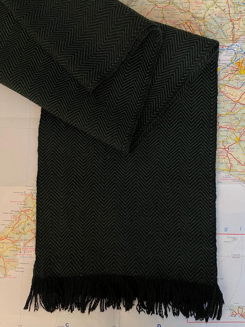 Puede incluir: Una bufanda verde oscuro con un dise&ntilde;o de espiga y un borde con flecos. La bufanda est&aacute; doblada, mostrando el tejido detallado. La bufanda est&aacute; hecha de un material suave y es adecuada para el clima fr&iacute;o.