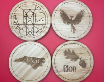 May include: Four round wooden coasters with laser-etched designs. The coasters feature a map of Elon, North Carolina, a phoenix, an oak leaf and acorn, and the word "Elon".
