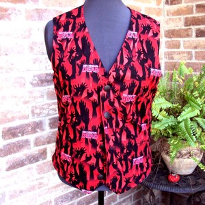 May include: A red vest with a black hand pattern and the text "This is the Dead". The vest has a V-neck and three black buttons down the front. The vest is displayed on a mannequin.
