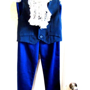 May include: A child's formal outfit, comprising a navy blue patterned waistcoat, a white lace collar, and matching blue trousers. The waistcoat has a single button and two small pockets.