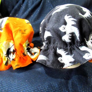 May include: Two Halloween-themed hats. One is orange with a black and white print, the other is black with white ghost figures. Both hats have a ruffled brim and are likely for costume wear.