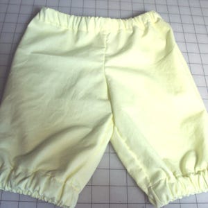 May include: A pair of pale yellow cotton shorts with a gathered elastic waistband and a gathered hem.