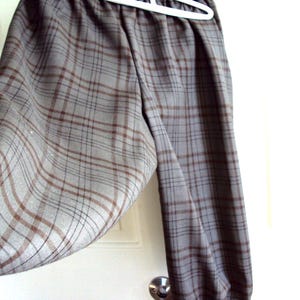 May include: Gray plaid pants hanging on a white hanger. The pants feature a classic plaid pattern in shades of gray and brown. The fabric appears to be a soft, woven material. The pants are hanging in front of a white door.