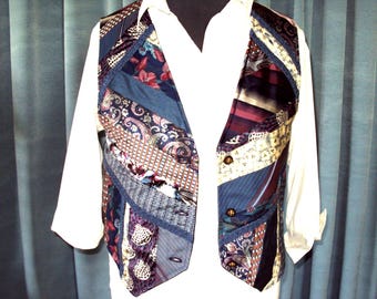 May include: A patchwork vest made from various patterned fabrics, including paisley, floral, and striped designs. The vest features a mix of colors, including blue, burgundy, and brown, and is accented with dark blue trim and gold-colored buttons. It is worn over a white collared shirt.