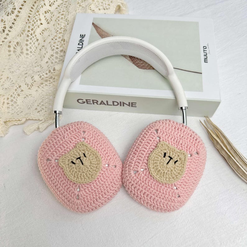 K&ouml;nnte beinhalten: Rosa geh&auml;kelte Ohrensch&uuml;tzer mit einem braunen B&auml;renkopf-Design. Die Ohrensch&uuml;tzer sind an einem wei&szlig;en Stirnband befestigt.