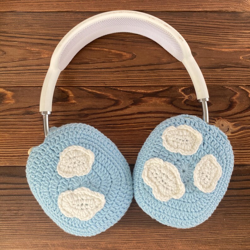 Puede incluir: Auriculares blancos con orejeras de ganchillo azul claro con dise&ntilde;os de nubes blancas.