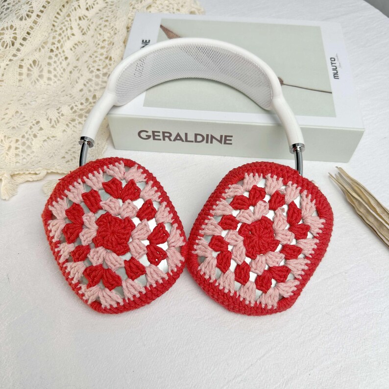 Op de afbeelding: Rode en roze gehaakte oorwarmers met een witte hoofdband. De oorwarmers hebben een granny square-patroon.