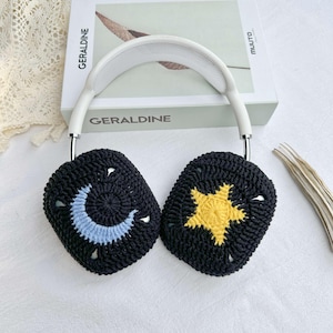 May include: White headphones with black crocheted ear covers. One ear cover has a blue crescent moon and the other has a yellow star.