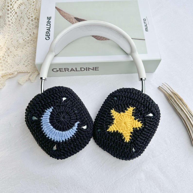 May include: White headphones with black crocheted ear covers. One ear cover has a blue crescent moon and the other has a yellow star.