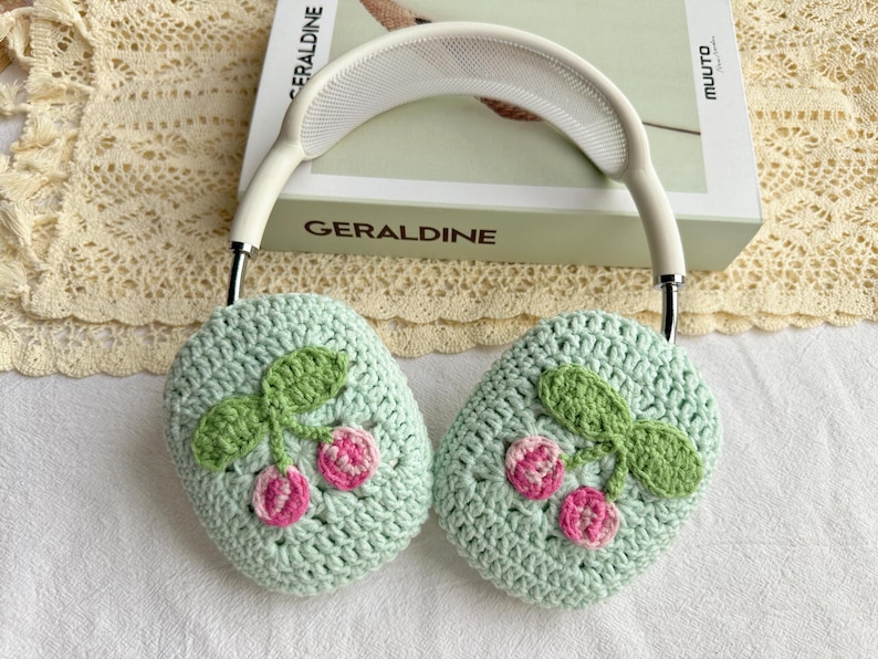 May include: Green crocheted headphone covers with a cherry design. The covers are attached to a white headband.