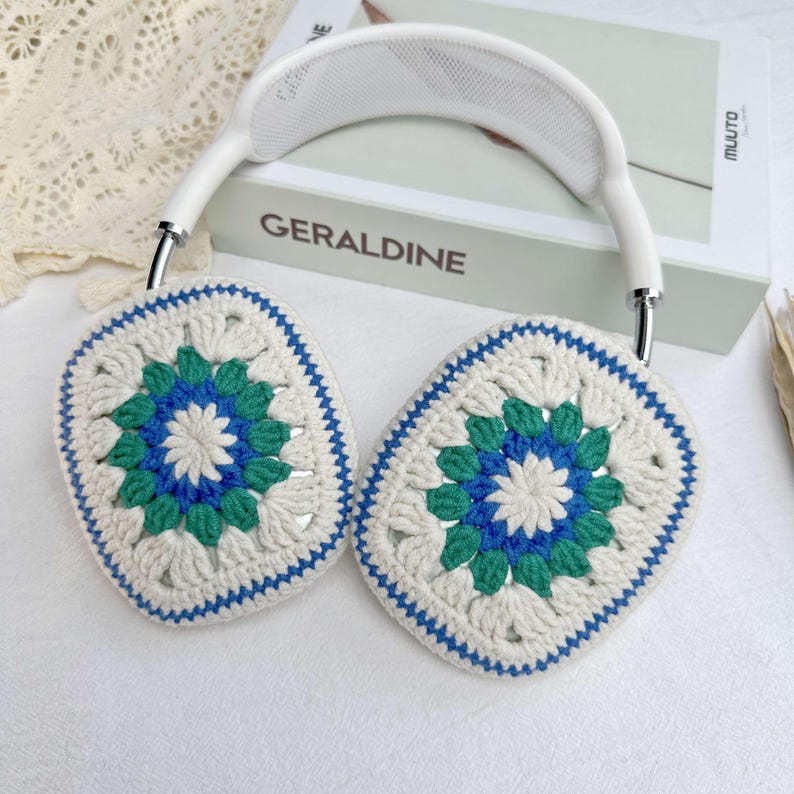 May include: White headphones with crocheted earmuffs. The earmuffs are white with blue and green accents and a floral pattern.