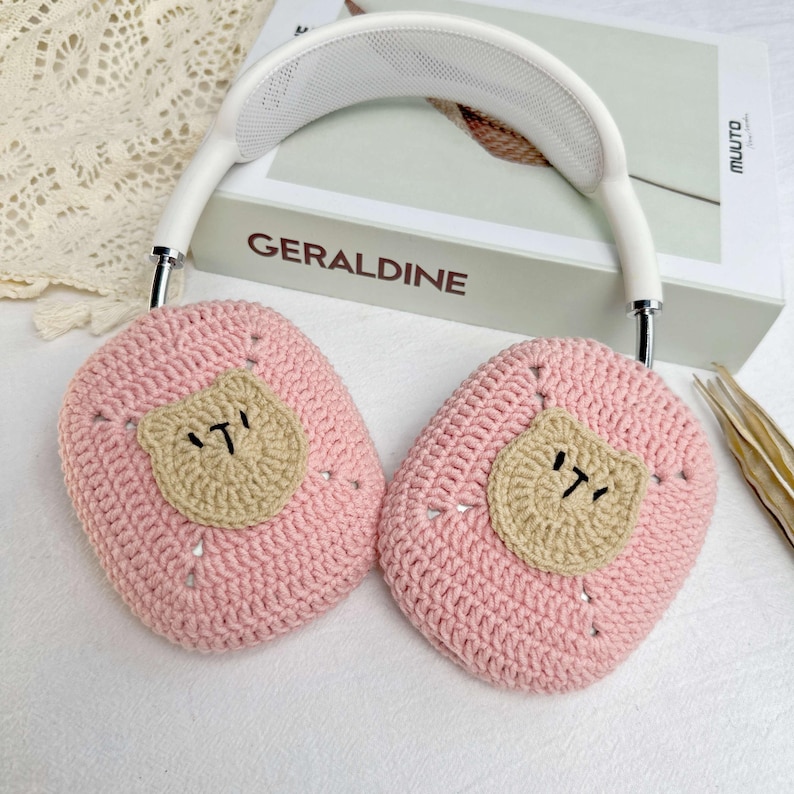 K&ouml;nnte beinhalten: Rosa geh&auml;kelte Ohrensch&uuml;tzer mit einem braunen B&auml;renkopf-Design. Die Ohrensch&uuml;tzer sind an einem wei&szlig;en Kopfband befestigt.