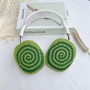 May include: White headphones with green and light green crocheted earmuffs. The earmuffs have a circular pattern.