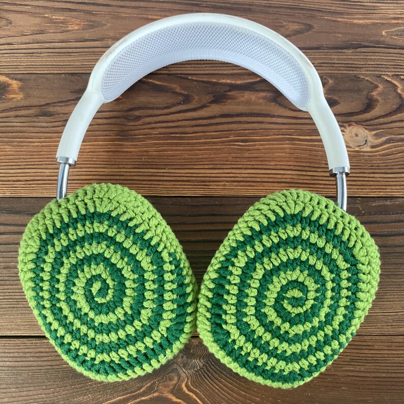 May include: White headphones with green crocheted ear covers. The ear covers have a circular pattern in shades of green.
