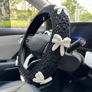 K&ouml;nnte beinhalten: Schwarze H&auml;kel-Lenkradabdeckung mit wei&szlig;en H&auml;kel-Schleifen.
