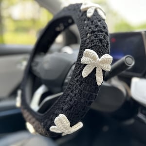 K&ouml;nnte beinhalten: Schwarze H&auml;kel-Lenkradabdeckung mit wei&szlig;en H&auml;kel-Schleifen.