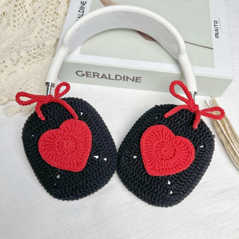 May include: Black crocheted headphone covers with red heart accents. The covers are attached to a white headband with a bow on each side.