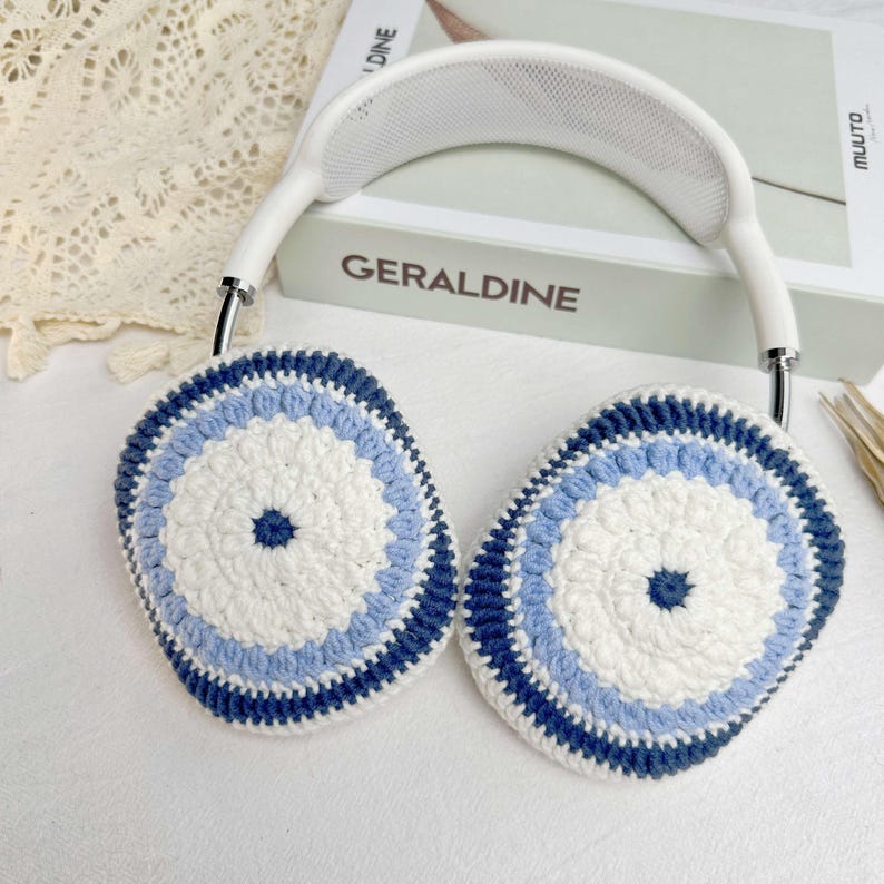 Puede incluir: Auriculares blancos con orejeras de ganchillo azul y blanco. Las orejeras tienen un patr&oacute;n circular con un centro azul.