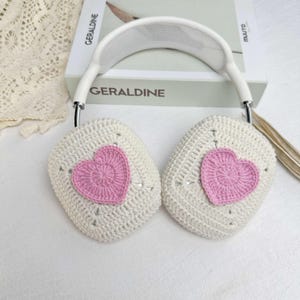 May include: White crocheted headphones with pink heart accents. The headphones are on a white surface.