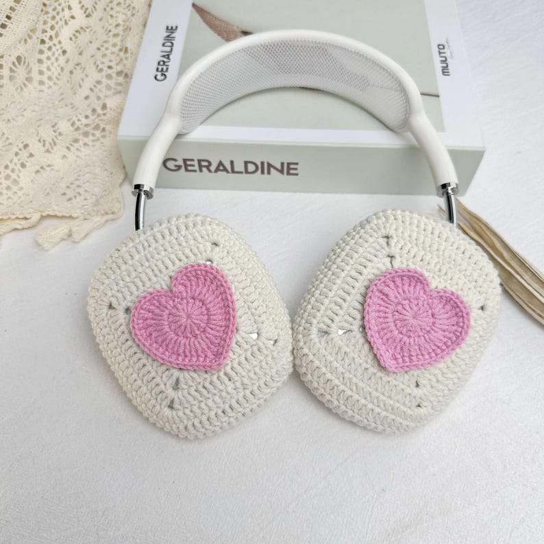 May include: White crocheted headphones with pink heart accents. The headphones are on a white surface.