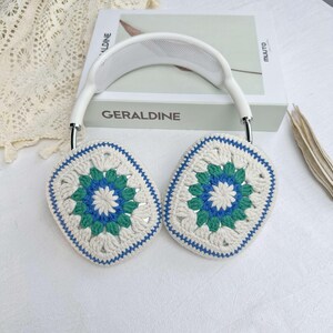 May include: White headphones with crocheted earmuffs. The earmuffs are white with a blue and green floral pattern.