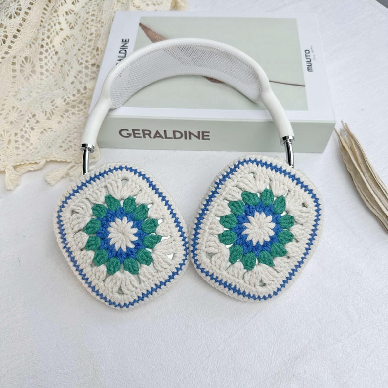 May include: White headphones with crocheted earmuffs. The earmuffs are white with a blue and green floral pattern.