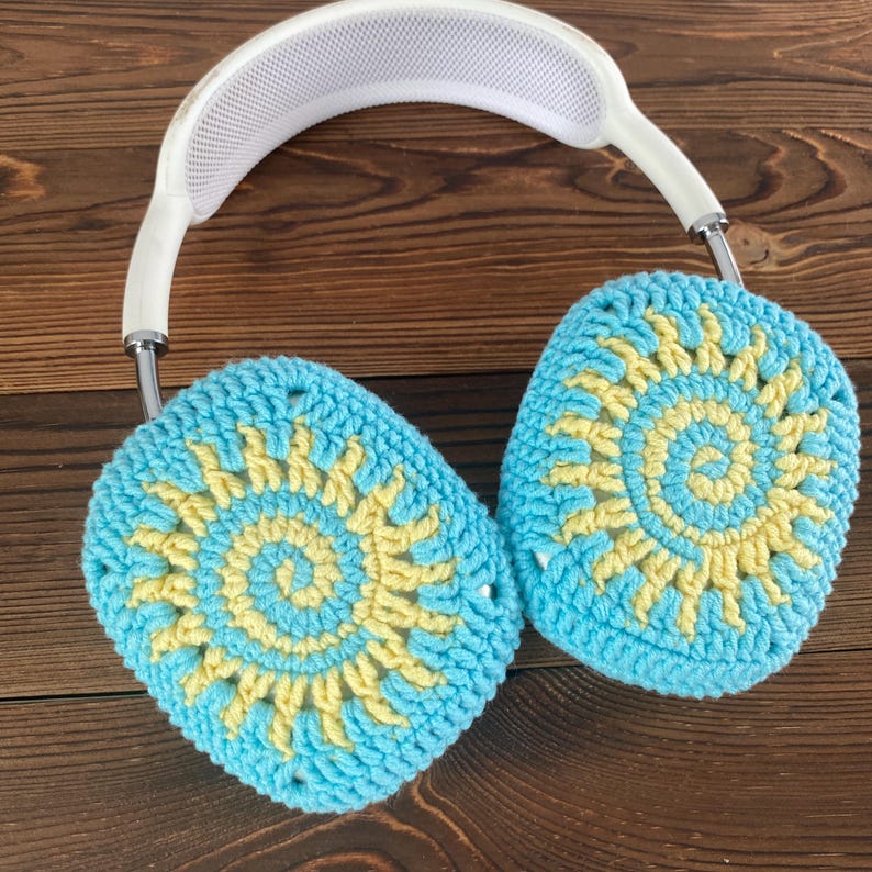 May include: White headphones with crocheted earmuffs. The earmuffs are blue and yellow with a sun design.