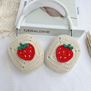 May include: White headphones with crocheted earmuffs featuring embroidered strawberry designs. The earmuffs are beige with red and green strawberries.