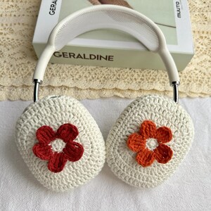 Puede incluir: Cubiertas de auriculares de crochet blanco con detalles de flores naranja y rojo.