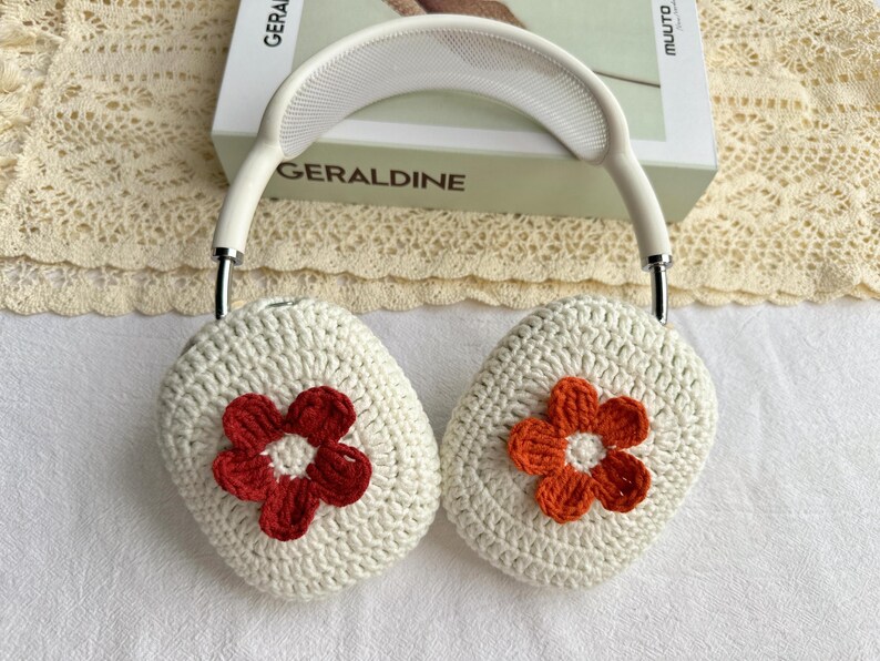 Puede incluir: Cubiertas de auriculares de crochet blanco con detalles de flores naranja y rojo.