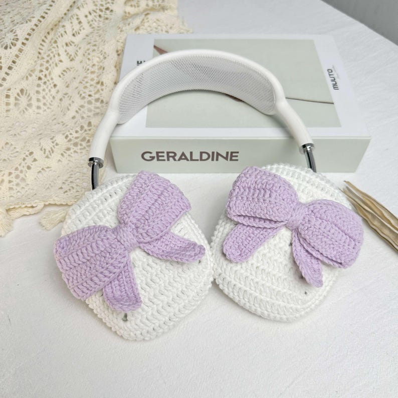 Puede incluir: Calentadores de orejas de crochet blanco con lazos de crochet morado. Los calentadores de orejas est&aacute;n unidos a una diadema blanca.