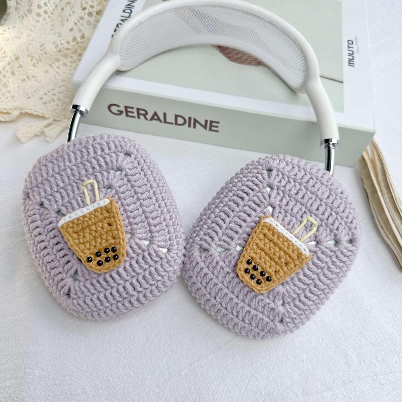 May include: Purple crocheted headphone covers featuring a boba tea design. The covers are crafted from soft yarn and have a charming, whimsical appearance.