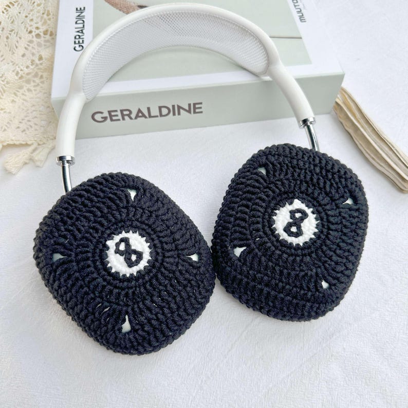 Puede incluir: Cubiertas de orejas de crochet negras con un c&iacute;rculo blanco y un dise&ntilde;o de n&uacute;mero ocho, unidas a una diadema blanca.