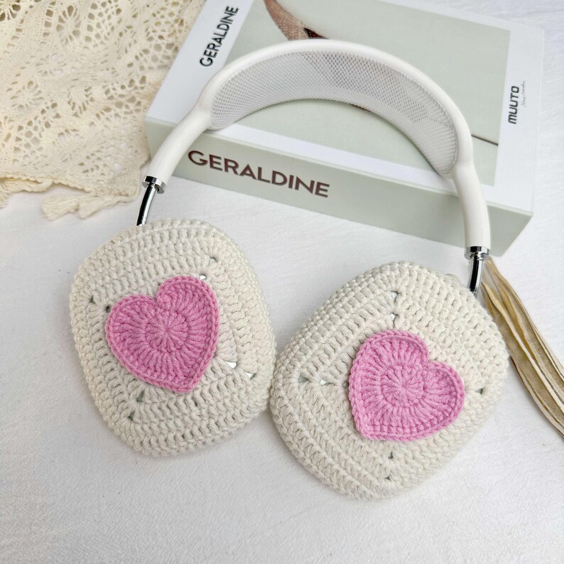 May include: White crocheted headphones with pink heart accents. The headphones have a white headband and a white mesh design on the inside of the headband.