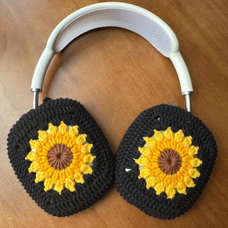 May include: Black crocheted earmuffs with sunflower designs. The earmuffs are attached to a white headband.