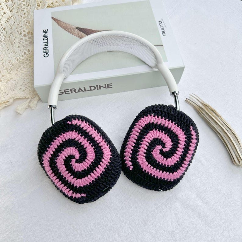 May include: White headband headphones with pink and black crocheted earmuffs featuring a spiral pattern.